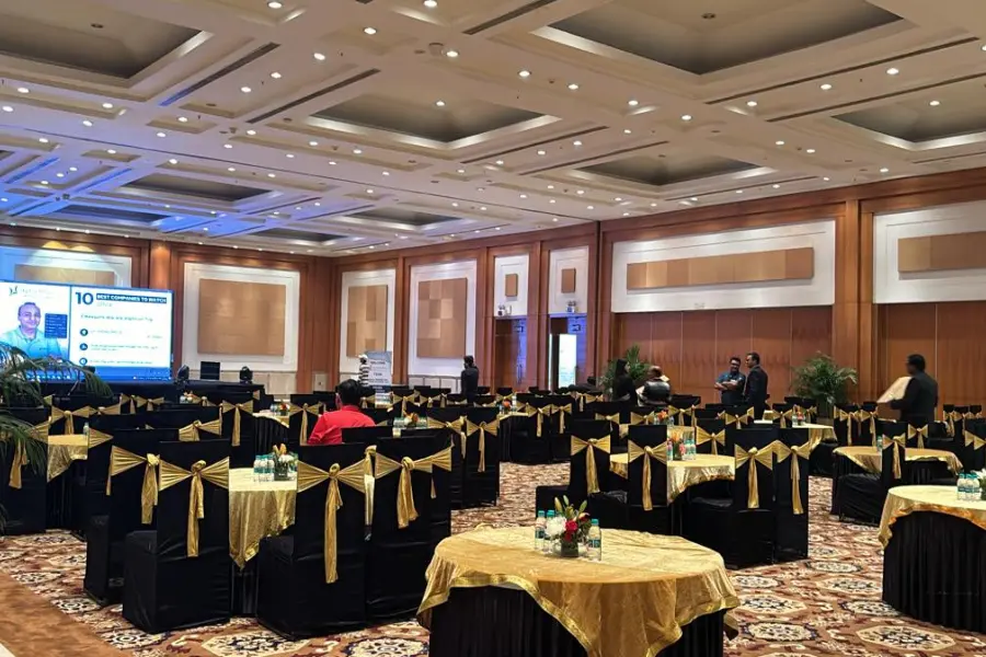 Banquet hall arranged for a corporate event with black chairs, gold sashes, and round tables set for dining.